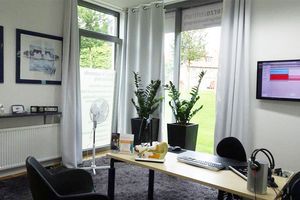Modernes, helles Büro mit Schreibtisch, Computer, Pflanzen und großem Fenster im Hintergrund.