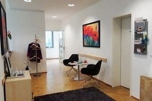 Heller Wartebereich mit modernen schwarzen Sesseln, Garderobe und bunter Wandkunst.